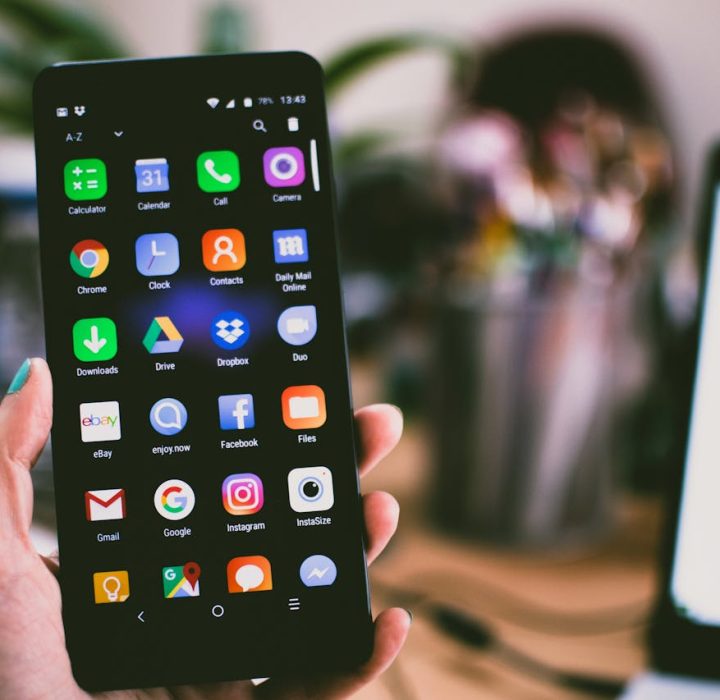 A close-up image of a person's hand holding a smartphone displaying various popular apps.