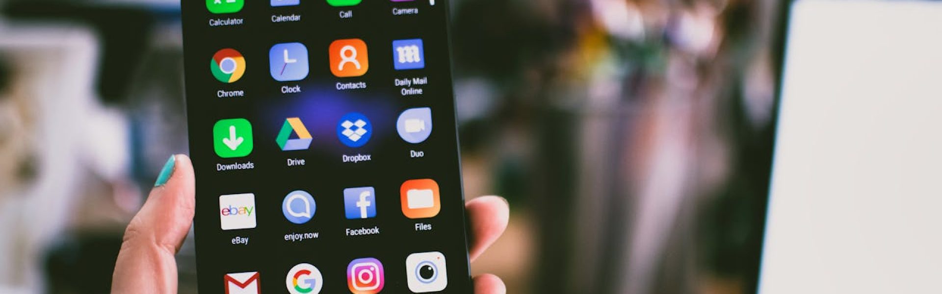 A close-up image of a person's hand holding a smartphone displaying various popular apps.